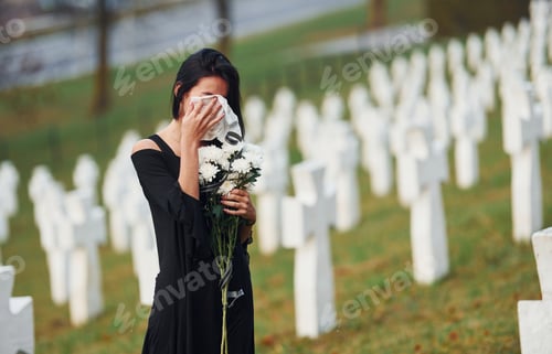 Preview: Young woman in black clothes visiting cemetery with many white crosses