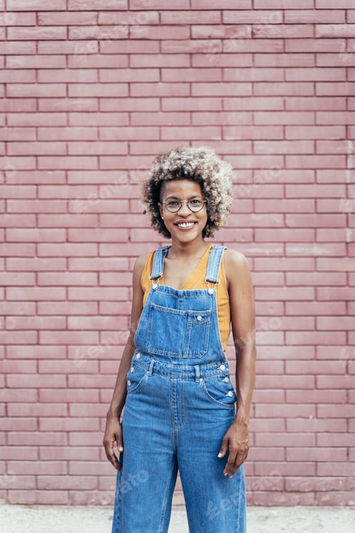 Preview: Portrait of a cool African American Woman with casual bib jeans overall over a brick wall