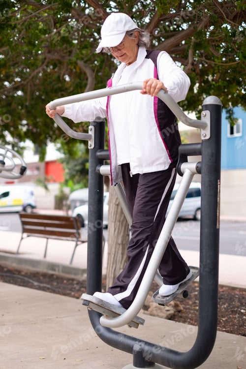 Preview: Active smiling retired woman exercising outdoors with sports free equipment in the park to keep fit