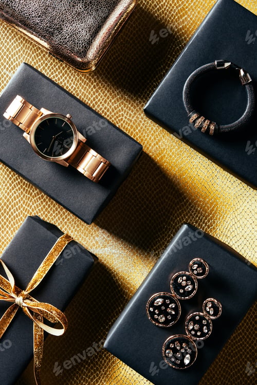 Preview: flat lay with wrapped gift, feminine jewelry and purse on golden backdrop