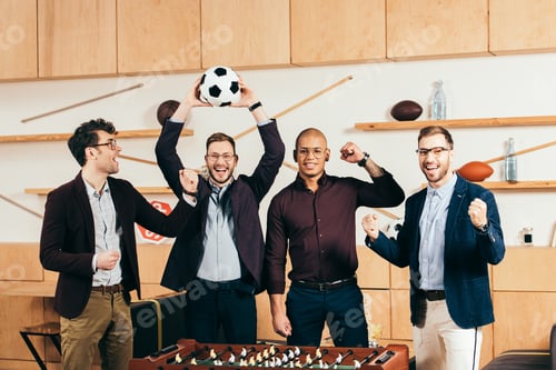 Preview: portrait of happy multiracial business team with soccer ball gesturing in cafe