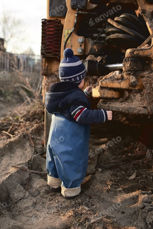 Preview: A boy in the village on the background of a tractor walks on the sand .