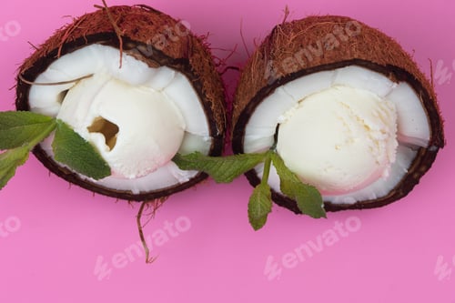 Preview: Vanilla ice cream balls in fresh coconut halves decorated with mint leaves on a pink background