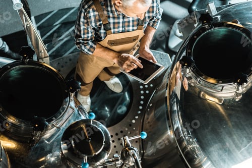 Preview: overhead view of male brewer using digital tablet and working in brewery