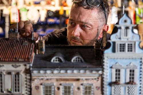 Preview: Model maker man working at scale model of miniature building in his workshop full of tools