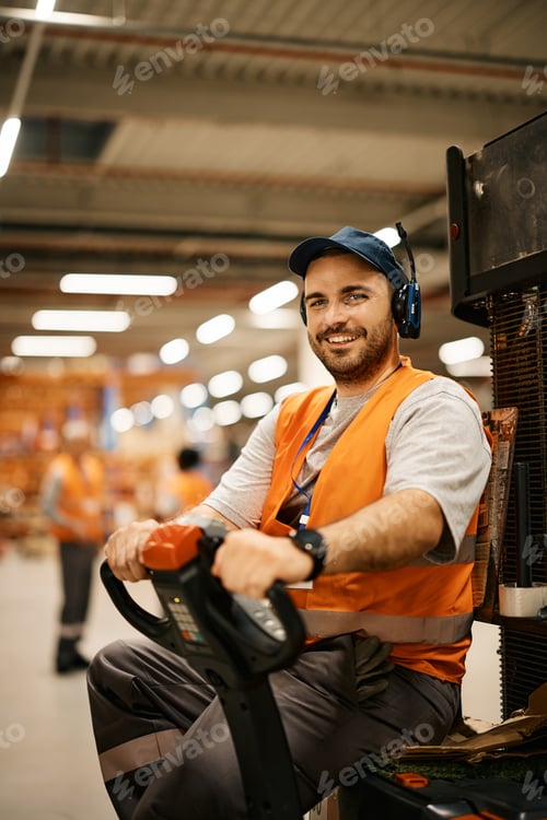 Preview: Happy male worker racking up packages with pallet jack in warehouse and looking at camera.
