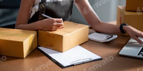 Preview: Woman entrepreneur prepare parcel box and check online order on laptop computer for commercial