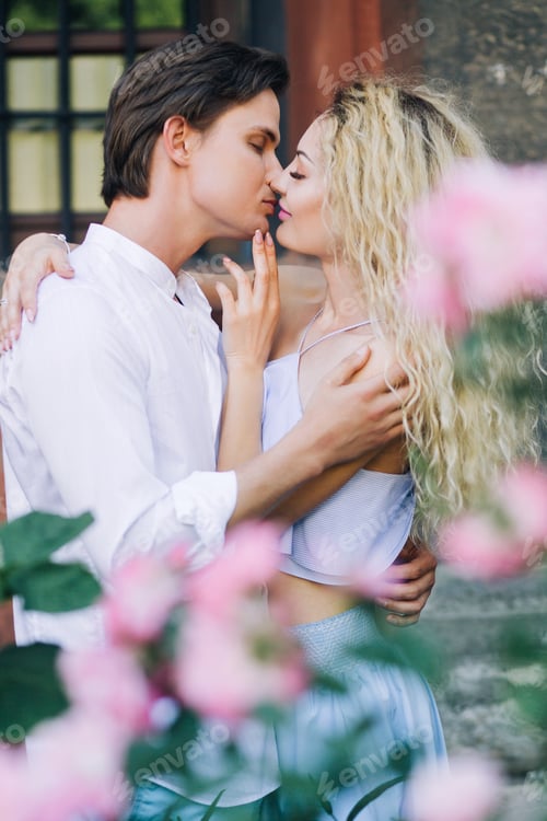 Preview: Young family couple on honeymoon in stylish summer clothes near pink flowers outdoors