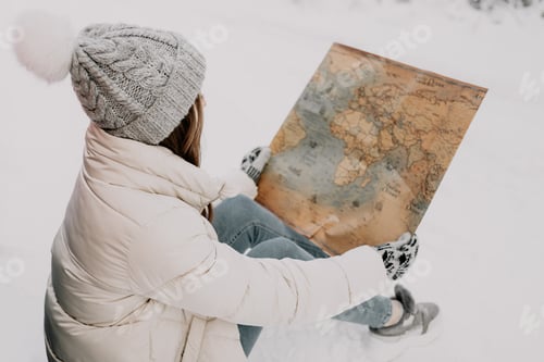 Preview: A young woman sits in the snow and holds a map in her hands. Travel concept.