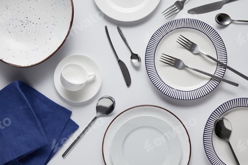 Preview: top view of different ceramic plates, cup, kitchen towel, forks, spoons and knife on white table