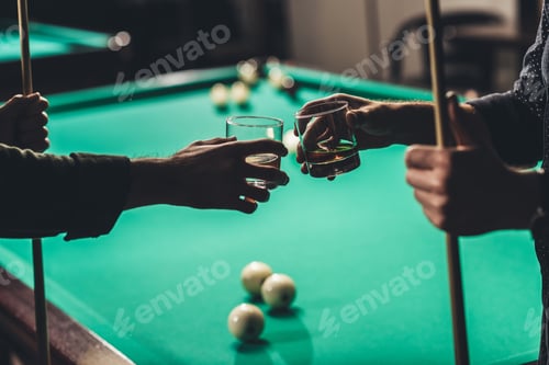 Preview: cropped image of male hands with cues and glasses with alcohol infront of billiard table at bar