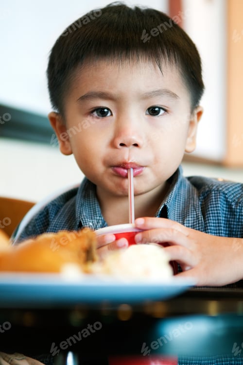 Preview: Portrait of a young Asian boy sipping soft drink with drinking straw.