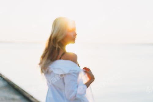 Preview: Beautiful blonde young woman in white shirt on pier on sunset