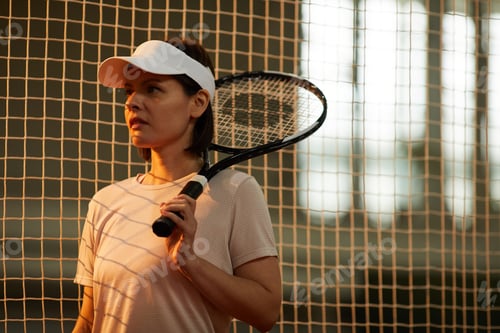 Preview: Young woman with racket standing by tennis net