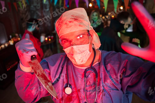 Preview: Creepy doctor with his covered holing a kinfe with blood and looking into the camera at halloween