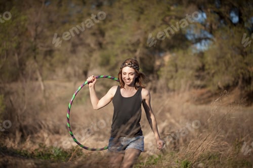 Preview: Young woman carrying hoola hoop in field