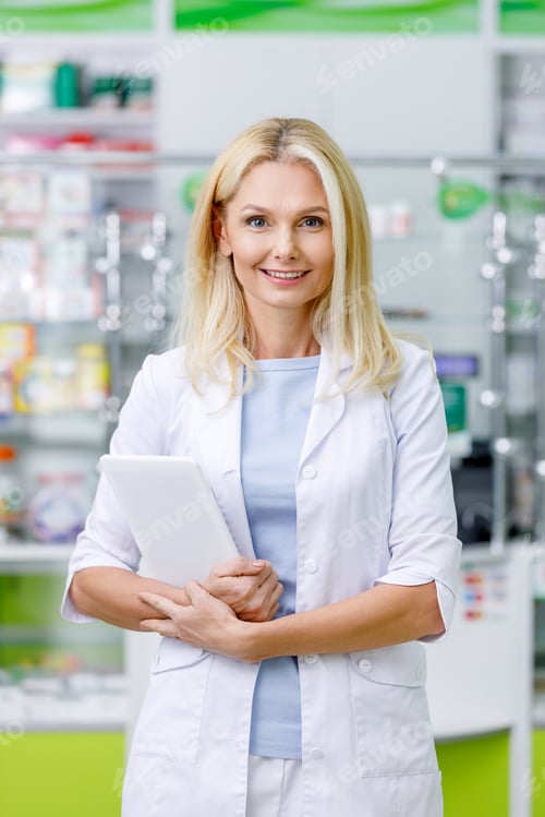 Preview: female pharmacist in white coat holding digital tablet and smiling at camera