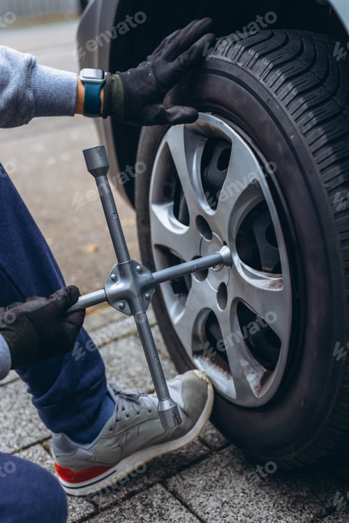 Preview: Man changing his car's tire with a wrench, replacing it with winter tires for the season