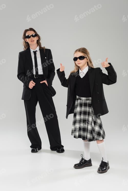 Preview: stylish schoolgirl in sunglasses and uniform showing thumbs up and standing near modern mother