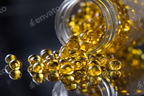 Preview: Yellow softgel scattered from transparent jar on greige ston, Nutritional supplements or vitamins