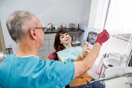 Preview: Senior male dentist in dental office talking with female patient and preparing for treatment