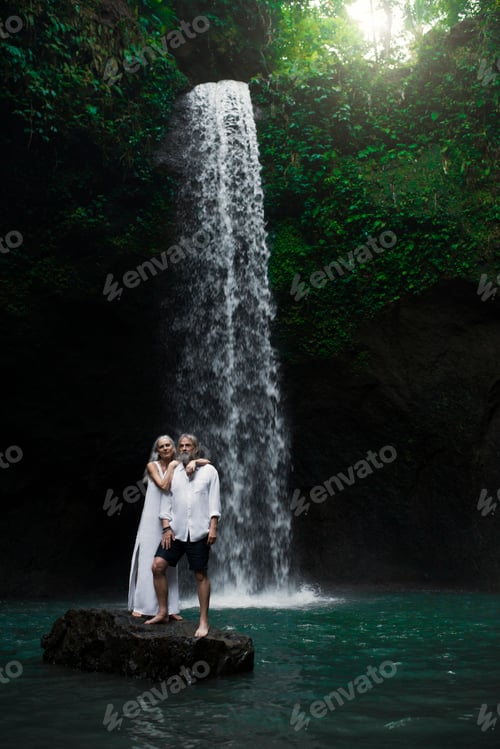 Preview: Affectionate senior couple standing in front of tropical waterfall