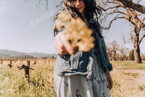 Preview: Woman in spring giving yellow flower in flower field