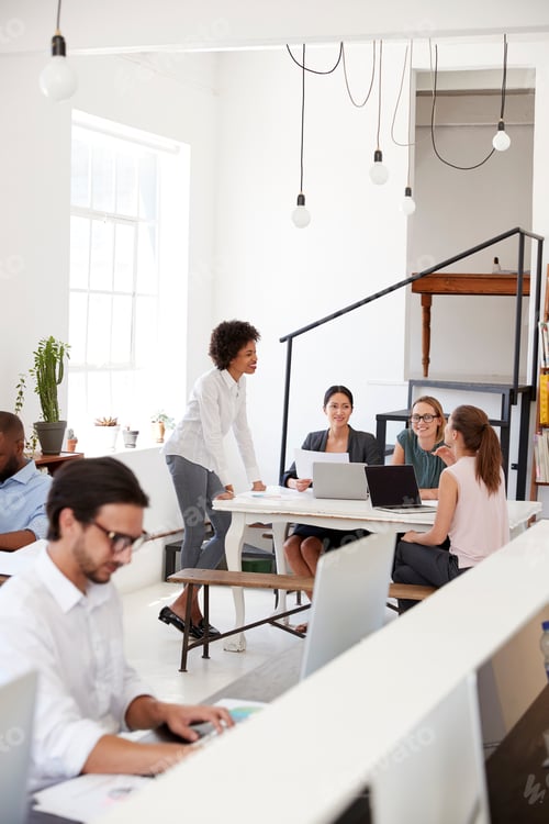 Preview: Woman briefing colleagues in an open plan office, vertical