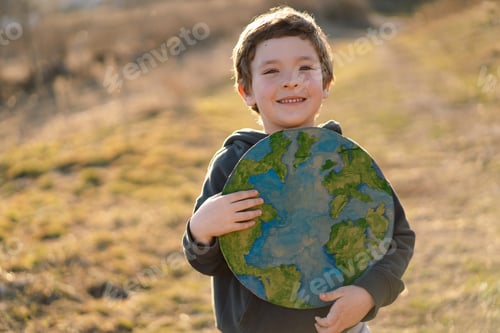 Preview: Little boy holding planet in hands against green spring background. Earth day