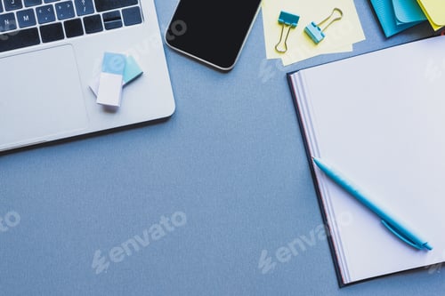 Preview: Top view of digital devices, stationery and open notebook on blue surface