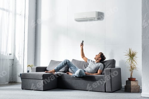 Preview: handsome man lying on sofa and switching on air conditioner
