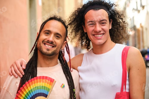 Preview: Gay couple smiling, looking at camera and holding a rainbow fan.