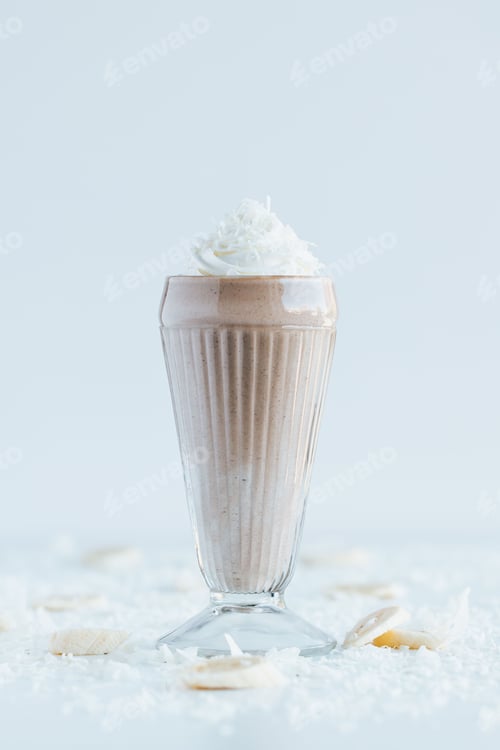 Preview: Vertical shot of the chocolate milkshake in a glass with coconut flakes on a white table