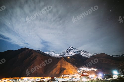 Preview: Stepantsminda, Georgia. Real Night Starry Sky With Glowing Stars Over Peak Of Mount Kazbek Covered