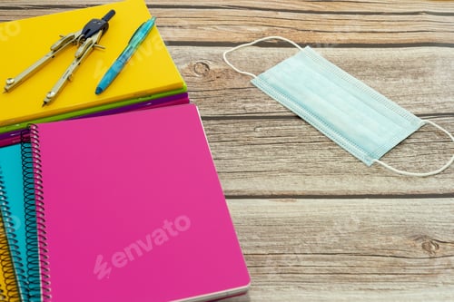 Preview: High angle shot of notebooks, sanitary mask, pen, compass on a wooden table