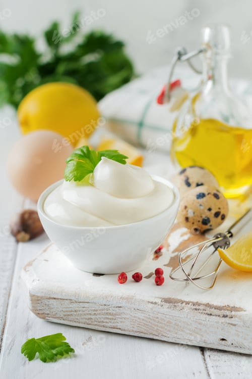 Preview: Traditional mayonnaise sauce in white ceramic bowl and ingredients for its preparation on white wood
