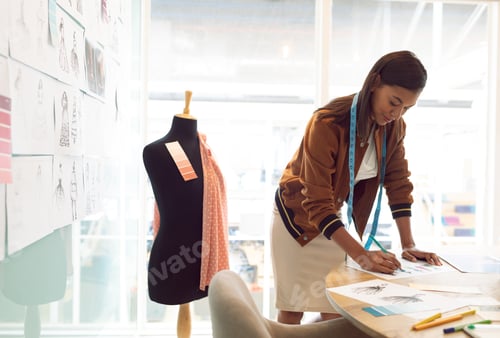Preview: Side view of beautiful mixed race female fashion designer drawing sketch on table in a modern office