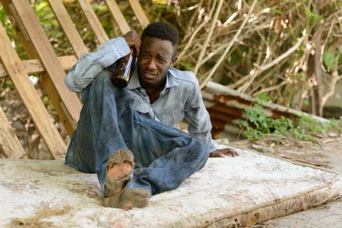 Preview: Sad young homeless African man getting drunk in the streets