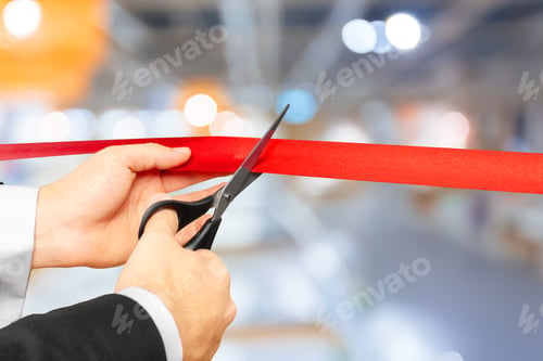 Preview: Businessman cutting red ribbon with pair of scissors
