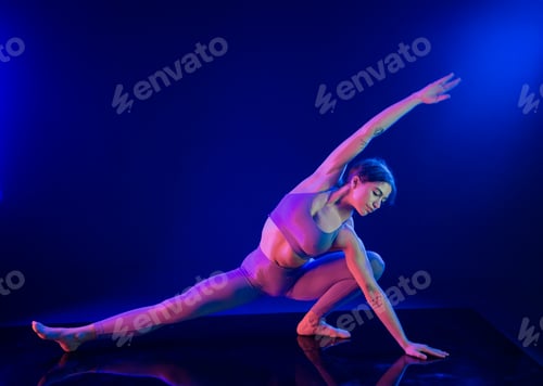 Preview: Woman in athletic wear performing a yoga pose under vibrant blue and purple lights.