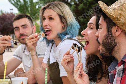 Preview: Group of happy friends smiling and eating sushi in a park having picnic.