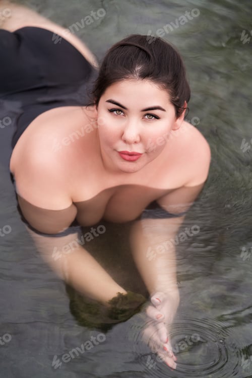 Preview: High angle shot of plus size woman with big breast in black swimsuit lying in outdoor pool at spa