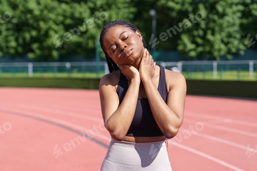 Preview: African American woman stretches body and neck preparing for running on track in sunny morning