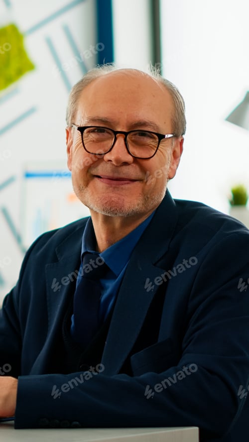 Preview: Elderly businessman looking at camera smiling sitting in brainstorming room