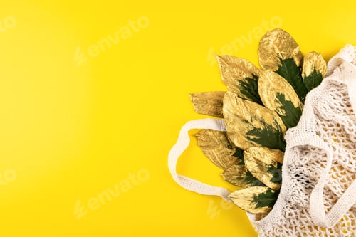 Preview: Reusable shopping net bag with green and golden leaves on yellow fall autumn background. Top view of
