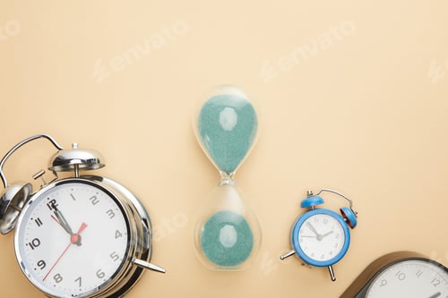 Preview: top view of classic alarm clocks and hourglass on beige background