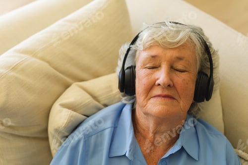 Preview: Senior caucasian woman sitting on sofa wearing headphones with eyes closed