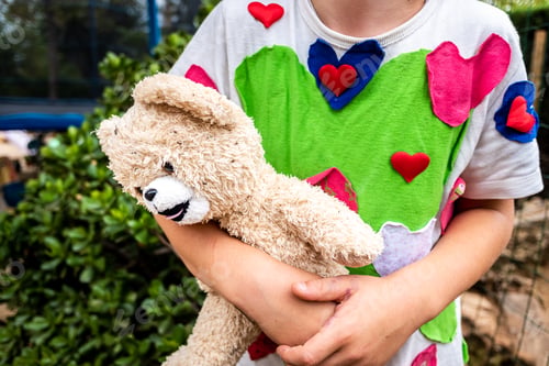 Preview: Strange scene of boy with hearts t-shirt holding a dirty and old teddy bear.