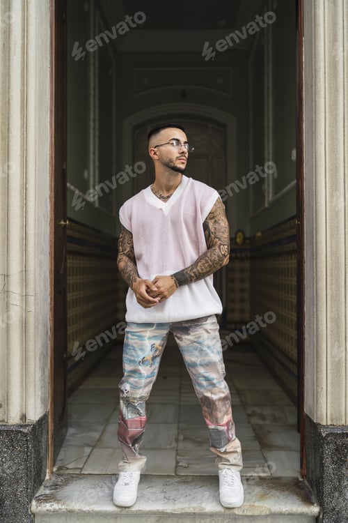 Preview: Hot caucasian man with arm tattoos wearing a white t-shirt and jeans posing at the entrance