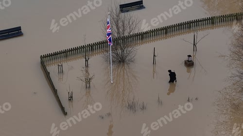Preview: two people are walking in flood waters in their yard and one is carrying an umbrella